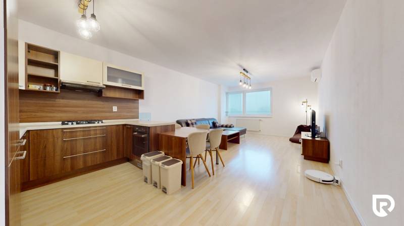 | Svetlý priestranný 2 izbový byt | parkovanie | REZERVOVANÝ - Obývacia izba s kuchynským kútom, podlahou s dreveným dekorom a pohovkou v 2-izbovom byte.