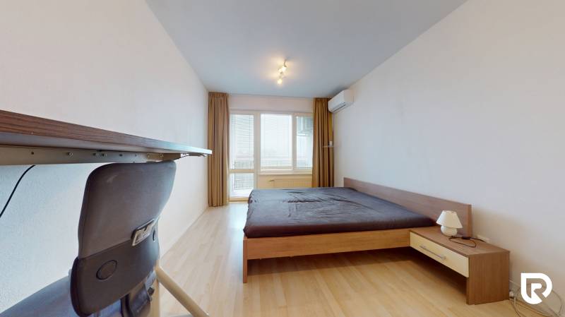 | Svetlý priestranný 2 izbový byt | parkovanie | REZERVOVANÝ - Spálňa v 2-izbovom byte s posteľou, stolom a podlahou s dreveným dekorom.