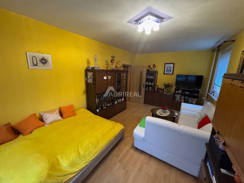 PREDAJ EXKLUZÍVNE: 1i byt s balk.; 41,02 m2; POPRAD; 124.200€ - Obývačka v 1-izbovom byte s bielou sedačkou a podlahou s dreveným dekorom.