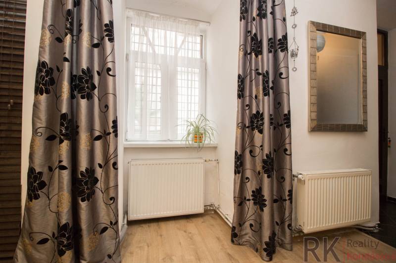 Centrum Košíc - 2-izb.tehlový byt s parkovaním vo dvore - Izba v 2-izbovom byte s podlahou s dreveným dekorom, závesmi a kvetinou na parapete.