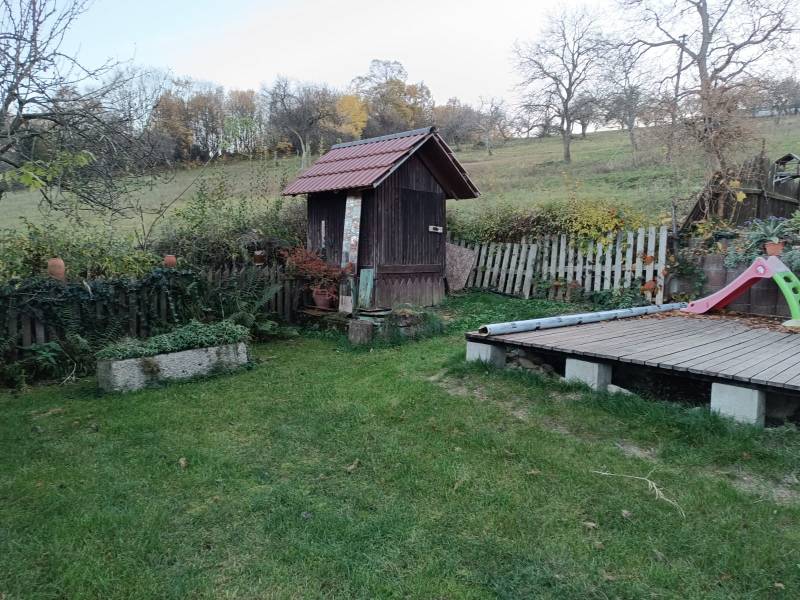 Samota Nová Baňa – Štále s hospodárskymi stavbami  - Záhrada s trávnikom a drevenou šmykľavkou, obklopená prírodou. V pozadí mierne svahy.