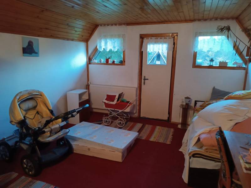 Samota Nová Baňa – Štále s hospodárskymi stavbami  - Izba v rodinnom dome s kočíkom, dreveným stropom a záclonami na oknách.