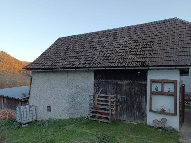 Samota Nová Baňa – Štále s hospodárskymi stavbami  - Na obrázku vidieť rodinný dom s drevenými dverami a sedlovou strechou na svahovitom pozemku.