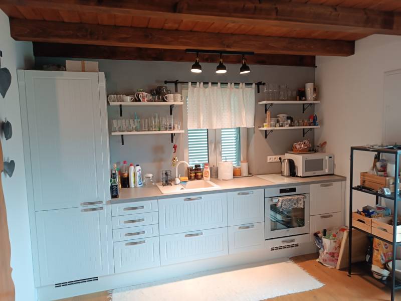 Rekreačná chata Nová Baňa - Drozdovo - Kuchyňa v chate s dreveným stropom, bielymi skrinkami, širokým oknom a otvorenými policami.