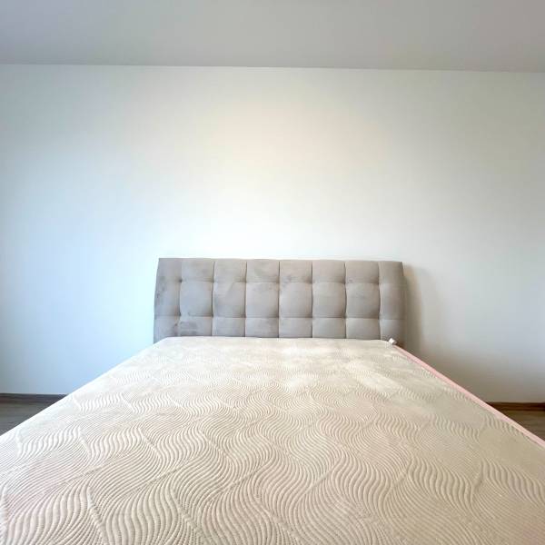 Súčasný 2-izbový byt v novostavbe – Matadorka  - Matrac s čalúneným čelom na posteli v dvojgarsónke, s podlahou s dreveným dekorom.