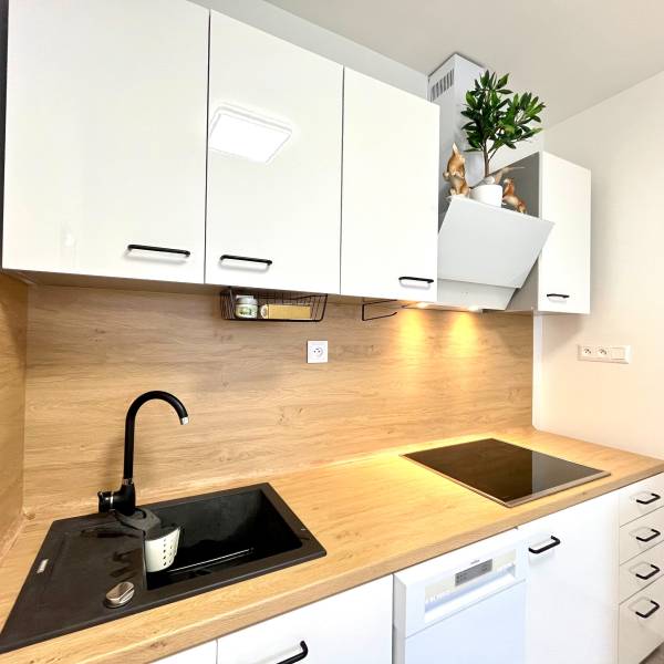 Súčasný 2-izbový byt v novostavbe – Matadorka  - Kuchynská linka v Dvojgarsónke s bielymi skrinkami a podlahou s dreveným dekorom.