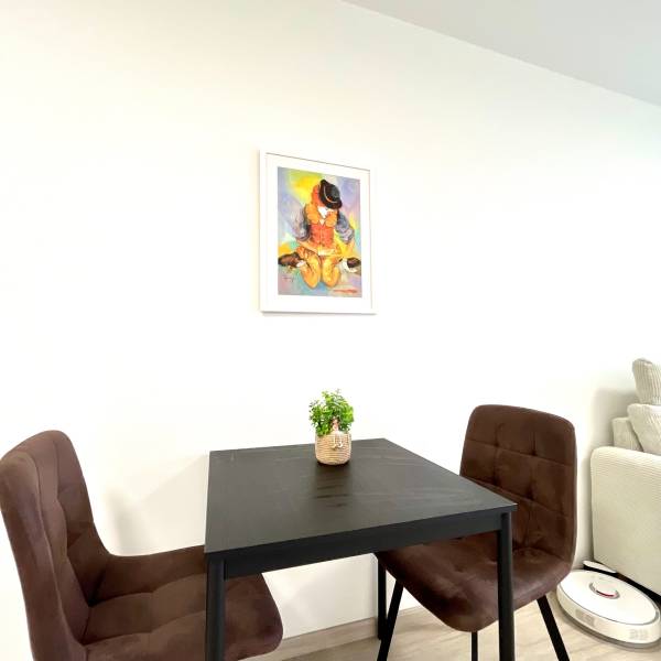 Súčasný 2-izbový byt v novostavbe – Matadorka  - Dvojgarsónka s jedálenským stolom, dvoma stoličkami a obrázkom na stene.