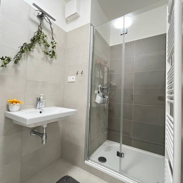 Súčasný 2-izbový byt v novostavbe – Matadorka  - Kúpeľňa v dvojgarsónke s jednoduchým umývadlom a sprchovým kútom so sklenenými dverami.