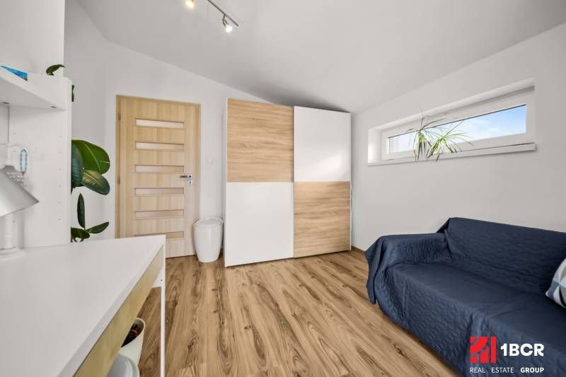 MODERNÝ 5-IZBOVÝ RODINNÝ DOM V ČUNOVE: 180m2 KOMFORTU A TICHA - Izba v rodinnom dome s podlahou s dreveným dekorom, skriňou a pohovkou.