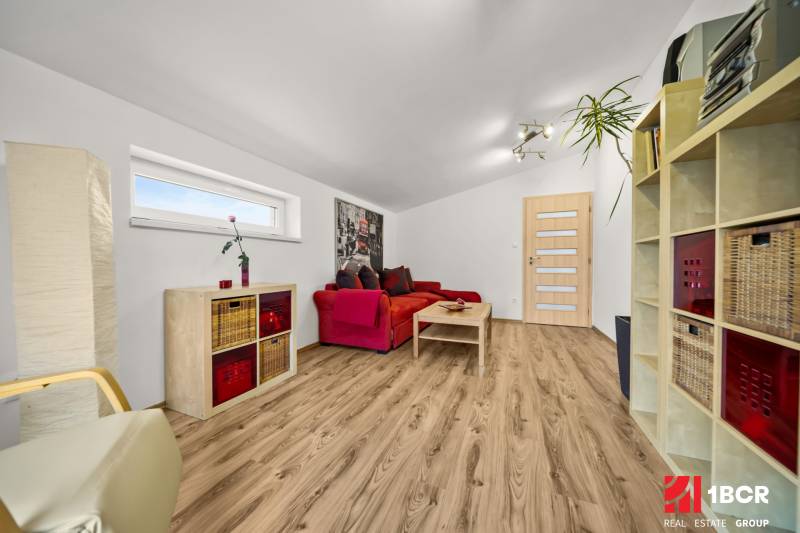 MODERNÝ 5-IZBOVÝ RODINNÝ DOM V ČUNOVE: 180m2 KOMFORTU A TICHA - Obývacia izba v rodinnom dome s červenou sedačkou a podlahou s dreveným dekorom.