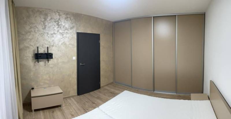 REZERVOVANÉ! Nadštandardný 1-izbový byt, ul. 1. mája, Vráble - Spálňa v 1-izbovom byte s podlahou s dreveným dekorom, vstavanou skriňou a TV držiakom.