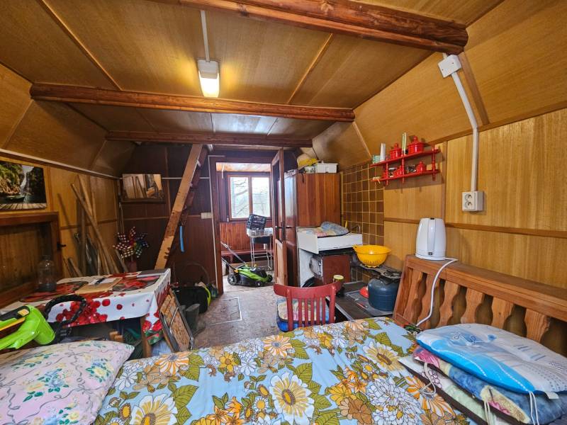 NA PREDAJ - ÚTULNÁ DREVENÁ CHATKA V DUBNICI NAD VÁHOM - Interiér chaty s dreveným dekorom, nábytkom a kuchynskými potrebami.