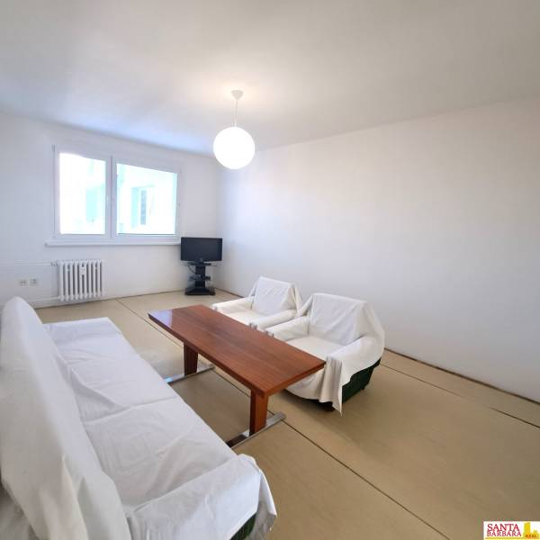 Na Predaj  4-izb. byt, Hornádska 28, Bratislava. - Obývačka so stolom a pohovkou v 4-izbovom byte, podlaha s dreveným dekorom.