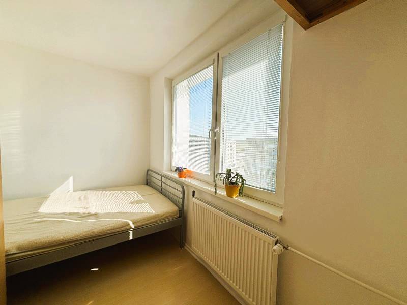 Slnečný dvojizbový byt – 43,5 m² v Bratislave – Vajnory - Svetlá spálňa s posteľou, oknom, žalúziami a podlahou s dreveným dekorom v 2-izbovom byte.