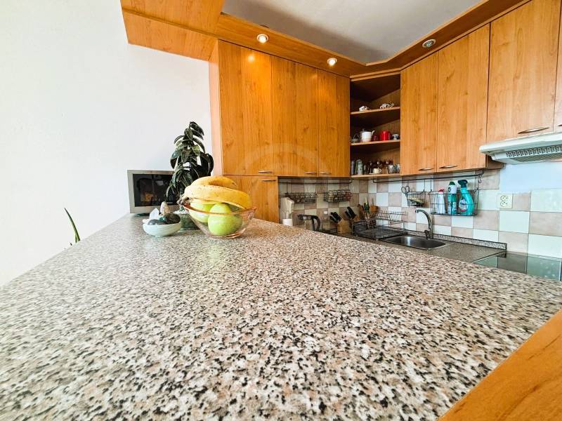 Slnečný dvojizbový byt – 43,5 m² v Bratislave – Vajnory - Kuchyňa v 2-izbovom byte s dreveným dekorom a ovocnou misou na kamennej doske.