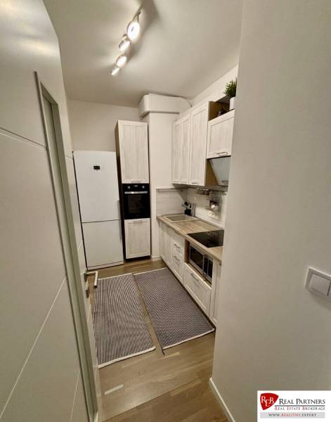 Prenájom 2-izbového bytu CUBICON  - Úzka kuchyňa v 2-izbovom byte s podlahou s dreveným dekorom a bielymi skrinkami.