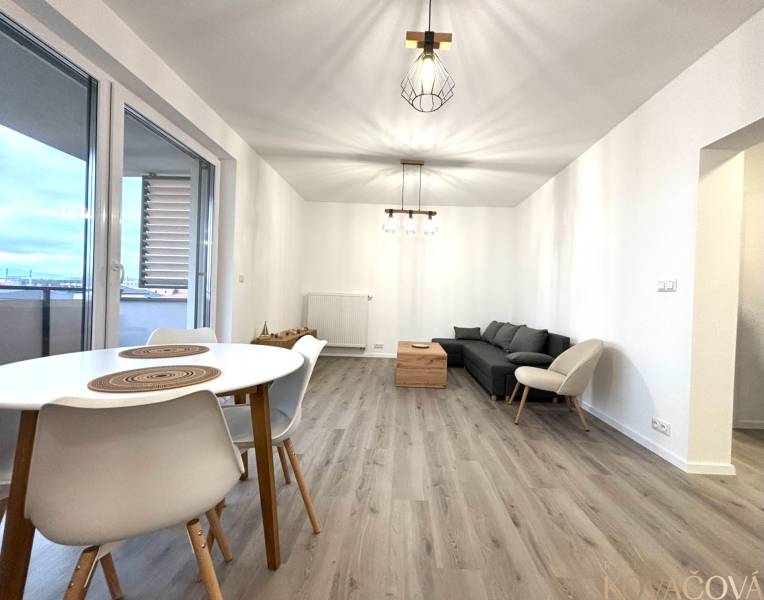 Na prenájom 3 izb. byt, Trenčín, ul.Vl.Predmerského, park.miesto,garáž - Obývačka v 3-izbovom byte s pohovkou, stolom a podlahou s dreveným dekorom.