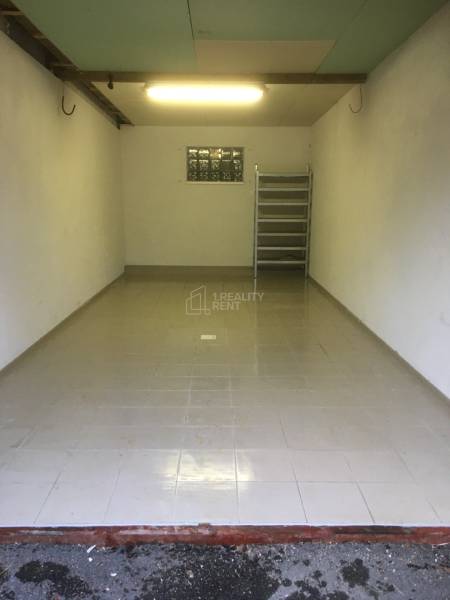 Predaj: Veľkometrážny 3+1 byt v Turzovke - Pohľad do prázdnej garáže so sivou dlažbou na podlahe a regálom vzadu.