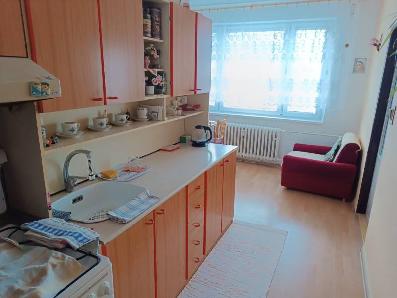 Na predaj veľkometrážny 3 izbový byt Žarnovica - Kuchyňa v 3-izbovom byte s podlahou s dreveným dekorom, vybavená skriňami a pohovkou.