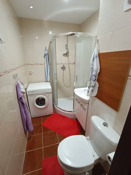 Na predaj veľkometrážny 3 izbový byt Žarnovica - Kúpeľňa v 3-izbovom byte, sprchový kút, práčka, toaleta a červené koberčeky.