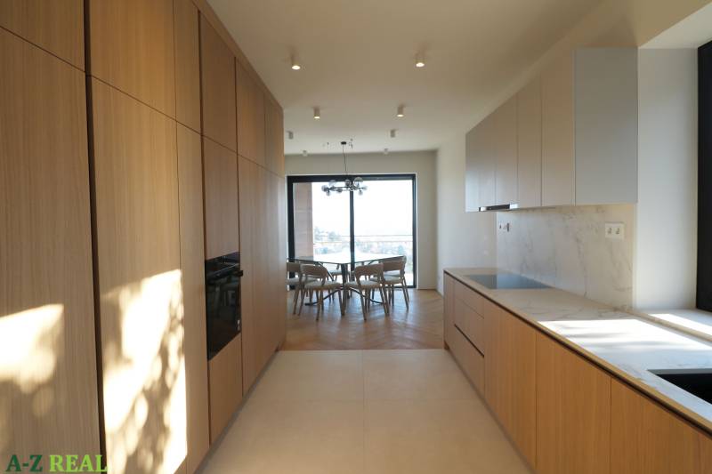 Prenájom 4 izbového bytu s krásnym výhľadom na mesto - Kuchyňa v 4-izbovom byte s podlahou s dreveným dekorom a svetlou kuchynskou linkou.