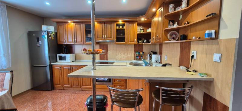 Predaj: Rodinný dom po rekonštrukcii s nadstavbou v Ochodnici (RCZ) - Kuchyňa v rodinnom dome s drevenými skrinkami, barovým pultom a spotrebičmi.