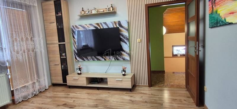 Predaj: Rodinný dom po rekonštrukcii s nadstavbou v Ochodnici (RCZ) - Obývacia izba v rodinnom dome s dreveným dekorom podlahy a veľkou televíziou na stene.