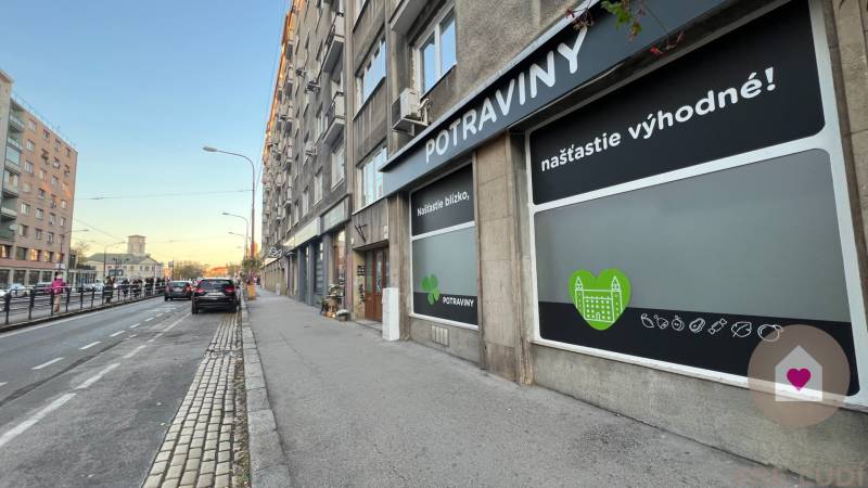 BA/STARÉ MESTO - Prenájom kompletne zariadeného 2i bytu s 2 balkónmi - Ulica Krížna v Bratislave, vedľa cesty sa nachádzajú potraviny s reklamnými nápismi.