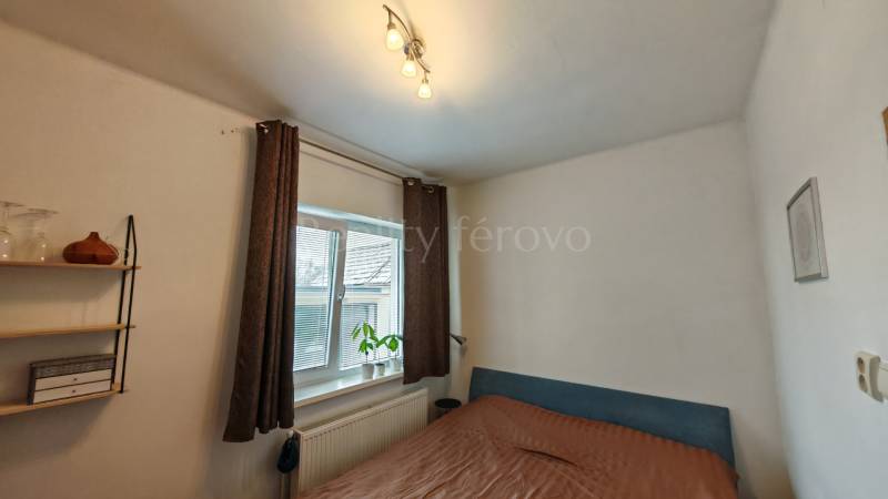 Na predaj rodinný dom v Trnovci nad Váhom - Spálňa v rodinnom dome, s posteľou, poličkami a oknom s dekoračnou rastlinou.