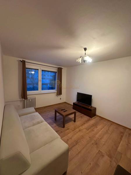 2-izb. byt, Nejedlého, Dúbravka, izby samostatné - Obývacia izba v 2-izbovom byte so sedačkou, televízorom a podlahou s dreveným dekorom.