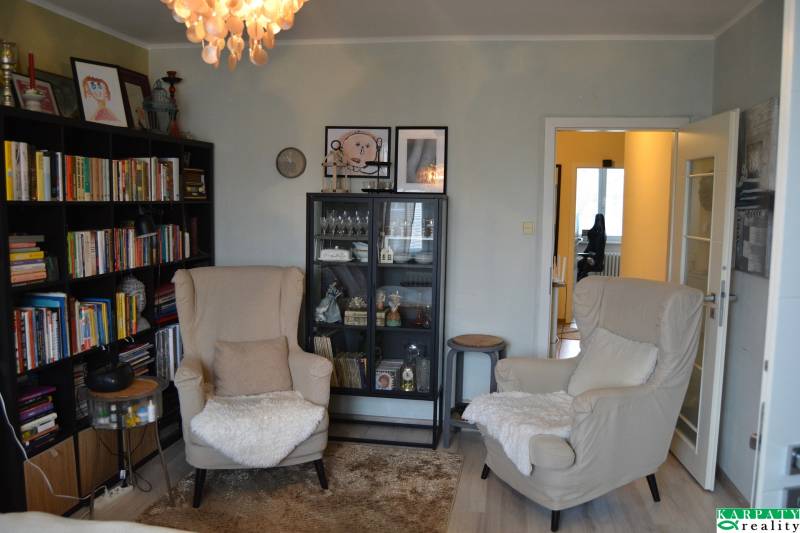 Útulný 3-izbový byt v Trnave na skok do Kamenáča! - Obývačka v 3-izbovom byte s policami na knihy a podlahou s dreveným dekorom.