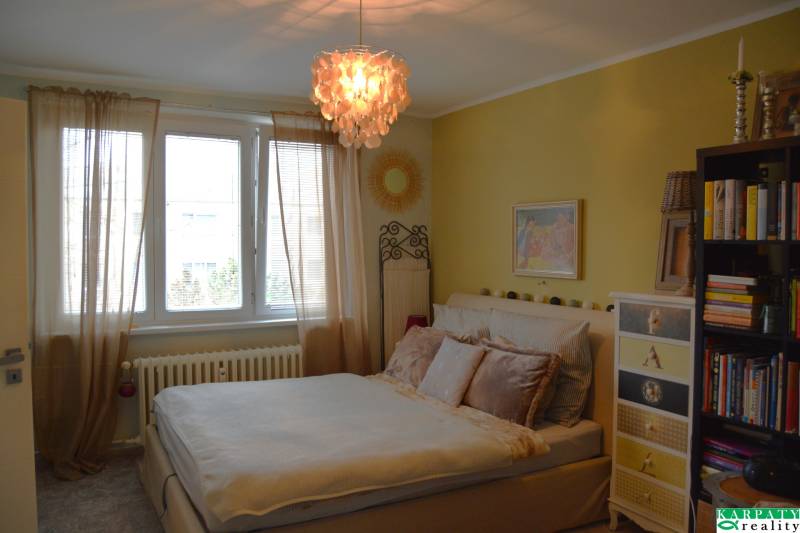 Útulný 3-izbový byt v Trnave na skok do Kamenáča! - Útulná spálňa so závesmi a knihovňou v 3-izbovom byte, atmosféru dotvára zaujímavý luster.