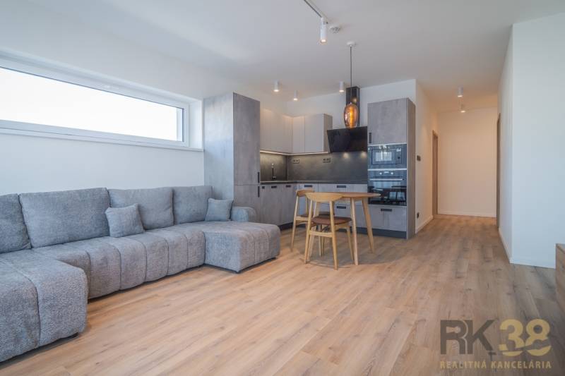 Na prenájom lukratívne 2-izbové byty v centre Popradu - Obývacia izba v 2-izbovom byte so sivou sedačkou a kuchyňou s dreveným nábytkom.