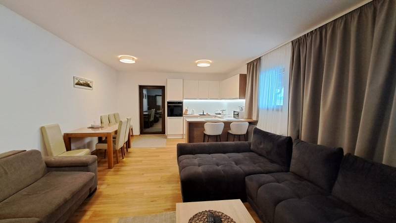 Lukratívny a priestranný 2-izbový apartmán v Mlynici na prenájom - Obývačka 2-izbového bytu s kuchyňou, jedálenským stolom a podlahou s dreveným dekorom.