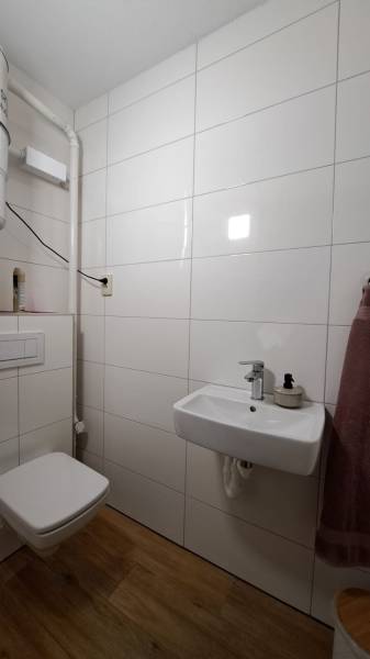 Lukratívny a priestranný 2-izbový apartmán v Mlynici na prenájom - Kúpeľňa v 2-izbovom byte s bielymi kachličkami a podlahou s dreveným dekorom.