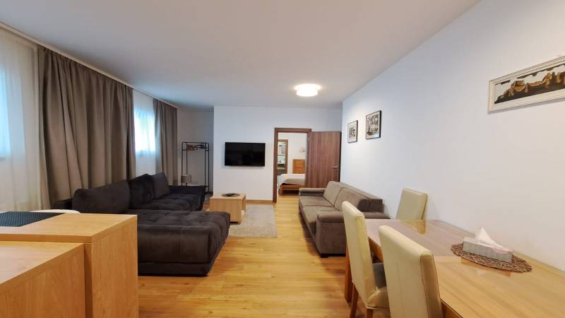 Lukratívny a priestranný 2-izbový apartmán v Mlynici na prenájom - Obývacia izba s pohovkou a TV, vedľa jedálenského stola, podlaha s dreveným dekorom.