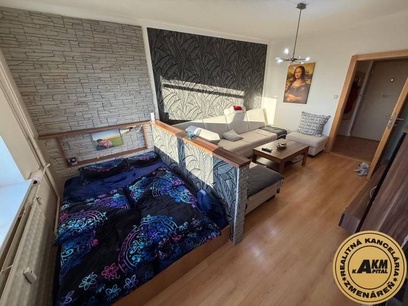 3 izbový byt 83 m² 2x balkón  Žiar nad Hronom centrum na predaj  - Obývacia izba s pohovkou, posteľou a podlahou s dreveným dekorom v 3-izbovom byte.