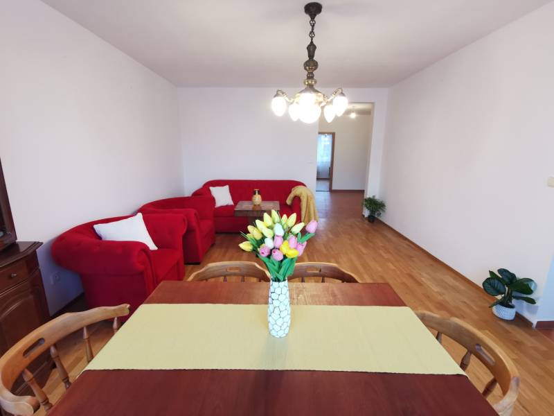 I Prenájom priestranného 4-izb.bytu, 2x balkón, parkovanie - 4-izbový byt s červeným sedením, jedálenským stolom a podlahou s dreveným dekorom.