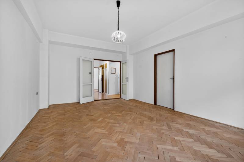 I PREDAJ Priestranný 3-izb. byt v centre Krížna/Blumentálska - Prázdna izba v 3-izbovom byte s podlahou s dreveným dekorom, bielymi stenami a lustrom.