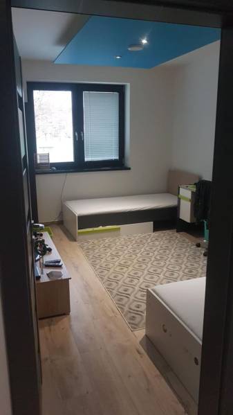 Predaj 4-izbového rodinného domu s veľkou záhradou v Semerove - Izba v rodinnom dome s podlahou s dreveným dekorom, postele, koberček a okno.