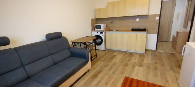 1-izbový byt na prenájom pri stanici – zariadený, po rekonštrukcii - Obývacia izba v 1-izbovom byte s pohovkou, kuchynským kútom a podlahou s dreveným dekorom.