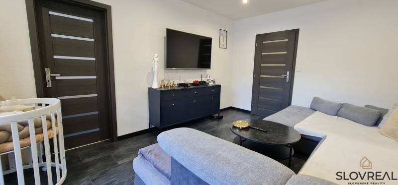 SLOVREAL - na predaj 2i byt Levice, 64m2 - Obývacia izba v 2-izbovom byte s tmavou podlahou a sedačkou.