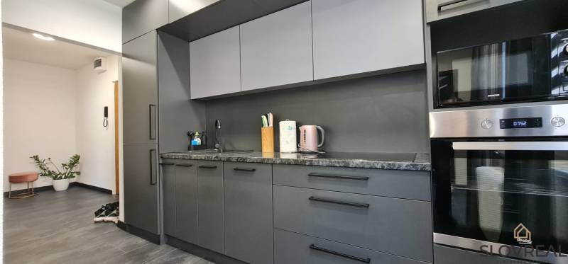 SLOVREAL - na predaj 2i byt Levice, 64m2 - Štýlová kuchyňa s modernými spotrebičmi a tmavým nábytkovým dekorom v 2-izbovom byte.