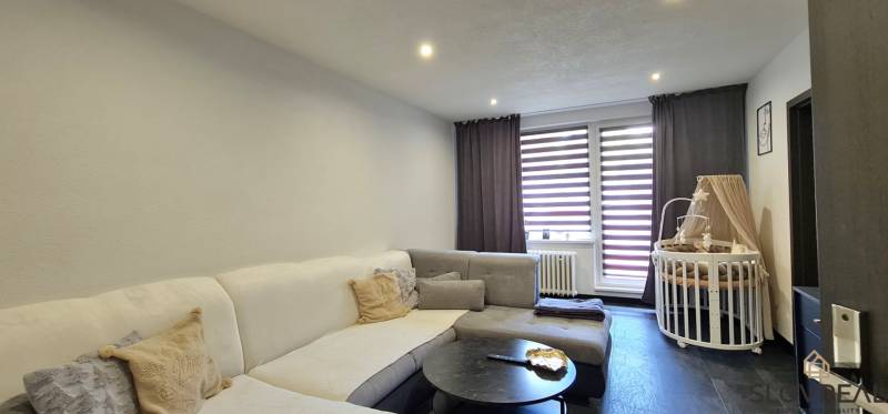 SLOVREAL - na predaj 2i byt Levice, 64m2 - Obývacia izba v 2-izbovom byte s pohovkou, konferenčným stolíkom a detskou postieľkou.