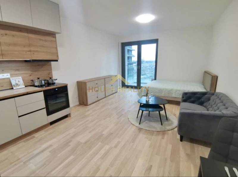 Prenájom novostavba 1 izb byt, Bottova ulica, Bratislava I Staré Mesto - Kuchynská linka, posteľ, gauč a podlaha s dreveným dekorom v 1-izbovom byte.