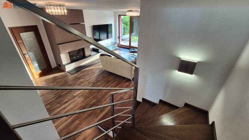 Reprezentatívny 5-izbový rodinný dom pri Piešťanoch - Obývacia izba s krbom a schodiskom v rodinnom dome, podlaha s dreveným dekorom.