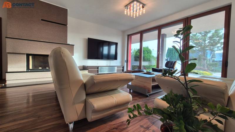 Reprezentatívny 5-izbový rodinný dom pri Piešťanoch - Obývačka Rodinného domu s koženou sedačkou, krbom, televízorom a podlahou s dreveným dekorom.