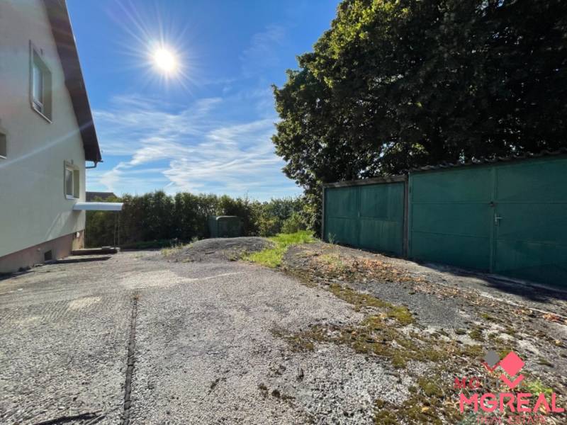 Veľký rodinný dom Podhradie  - Rodinný dom v Podhradí na Hlavnej ulici s garážou, stromom a betónovým povrchom.