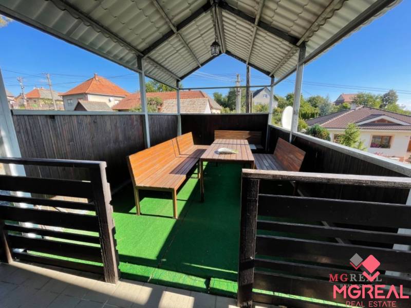 Veľký rodinný dom Podhradie  - Zastrešená terasa rodinného domu na Hlavnej ulici v Podhradí s dreveným sedením a umelým trávnikom.