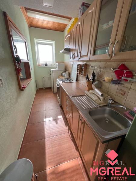 Veľký rodinný dom Podhradie  - Úzka kuchyňa v rodinnom dome s oknom a spotrebičmi, dominuje drevený dekor skriniek.